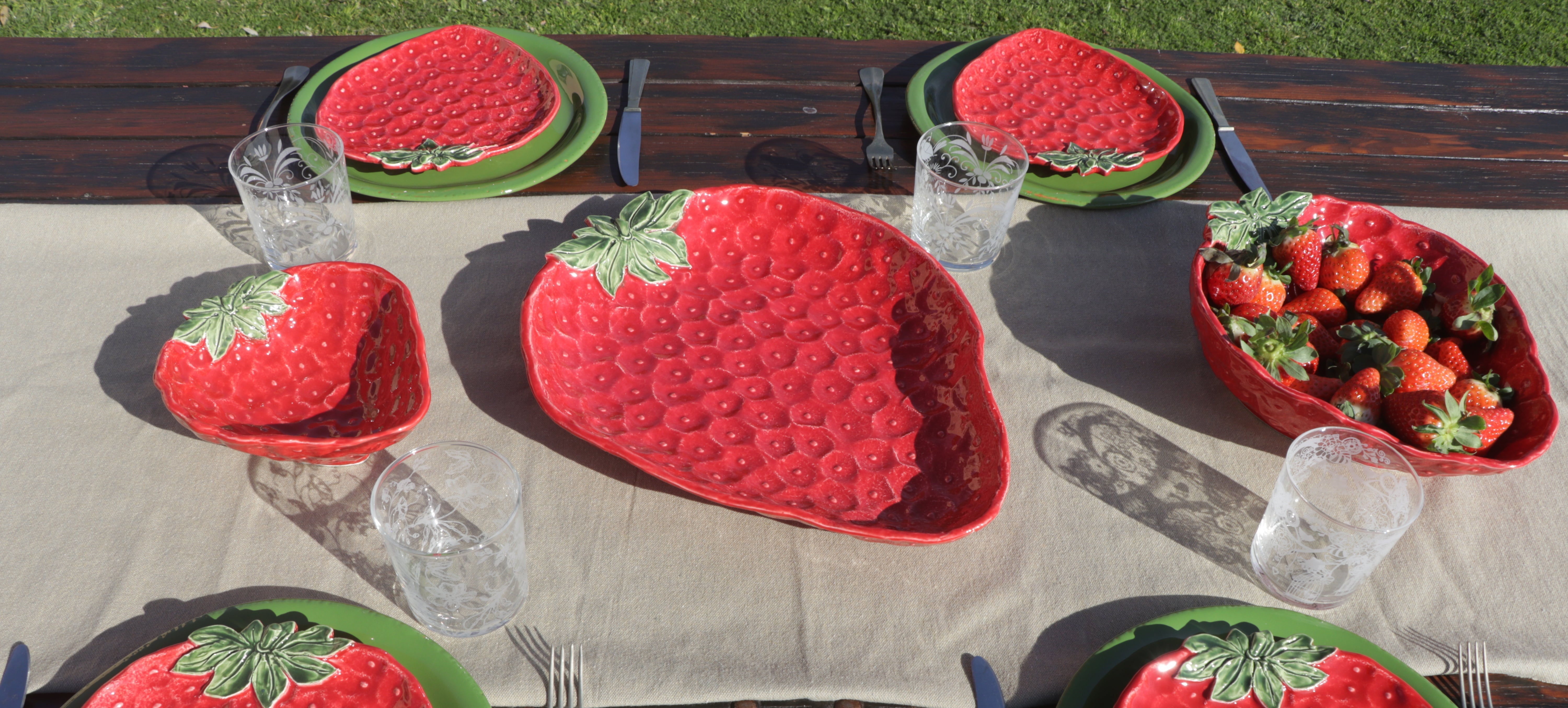 Table setting with strawberry-themed plates and bowls on a wooden table.